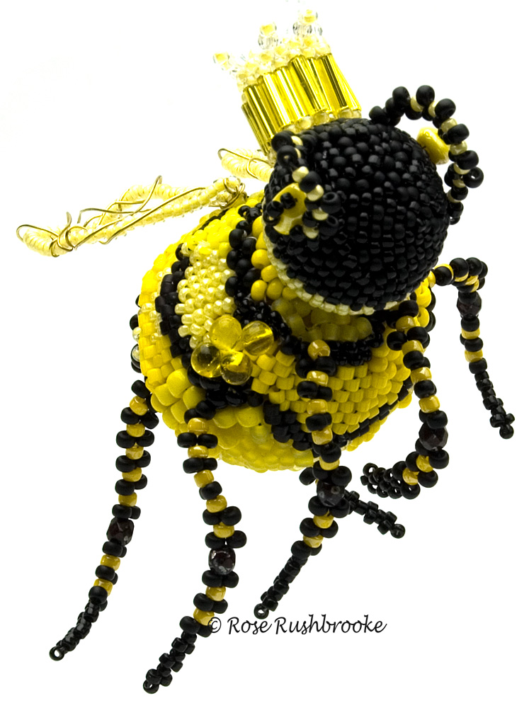The queen bee herself. Wooden beads covered in seed beads, wire wrapped wings, and seed bead antenna and legs. Image copyright &copy; Rose Rushbrooke.