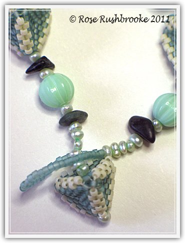 Close up of Triangles and Squares necklace clasp by Rose C Rushbrooke. Seafoam and cream beaded beads, pale blue dyed pearls, green opal chips, pink rondelles glass beads, and mint pressed glass beads. Peyote stitch beadweaving. Image copyright &copy; Rose C Rushbrooke.